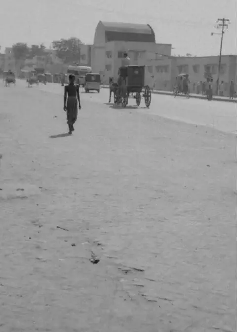A pedestrian and rickshaws on Mirpur Road, with the entrance to Government New Market behind them. Dhaka, 1966.