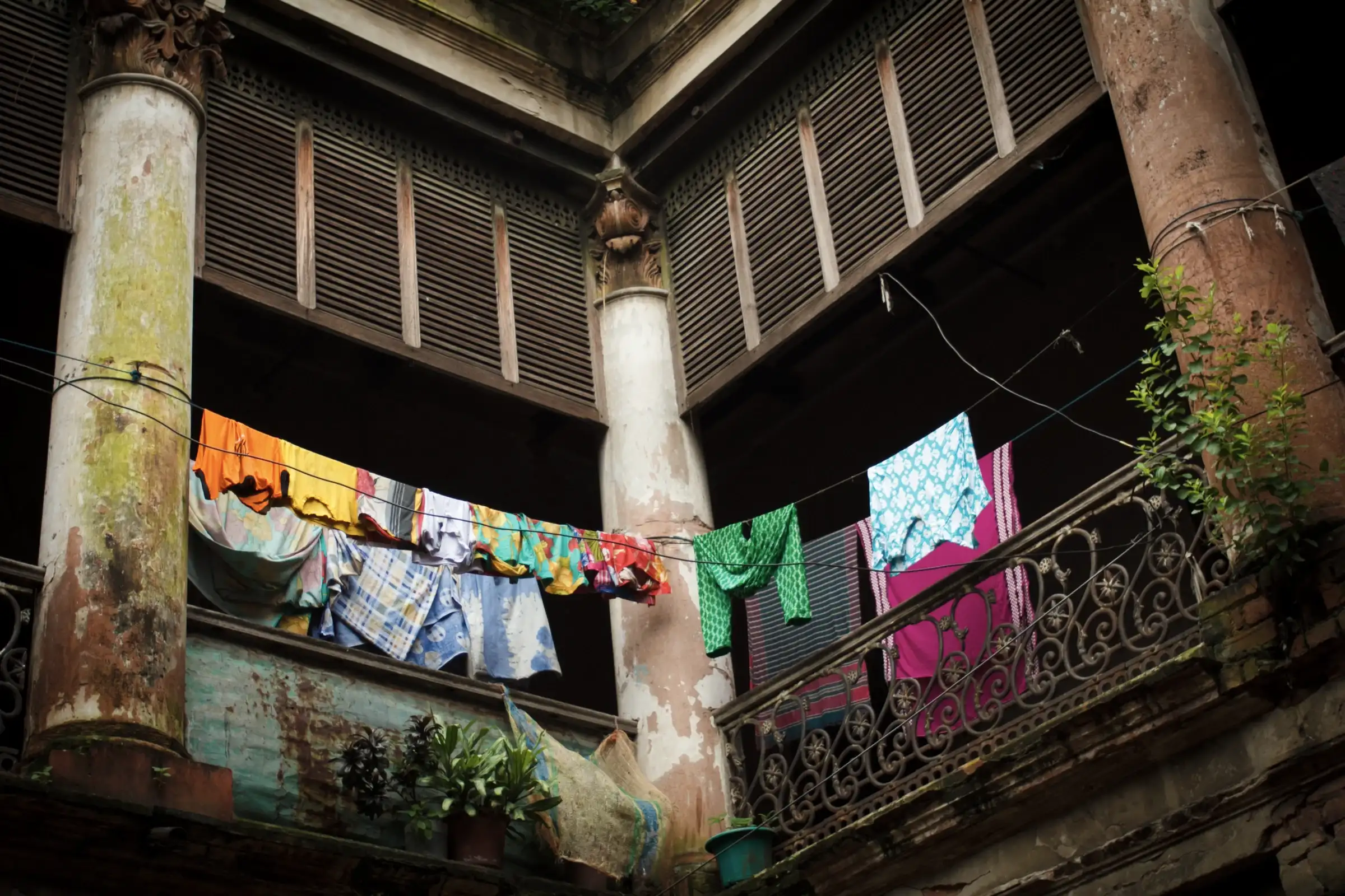Wooden shutters above a lived-in courtyard at Ruplal House, old Dhaka; washing hangs between weathered columns. Photographed in 2015.